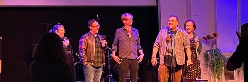 Five people are stood onstage, speaking to the audience