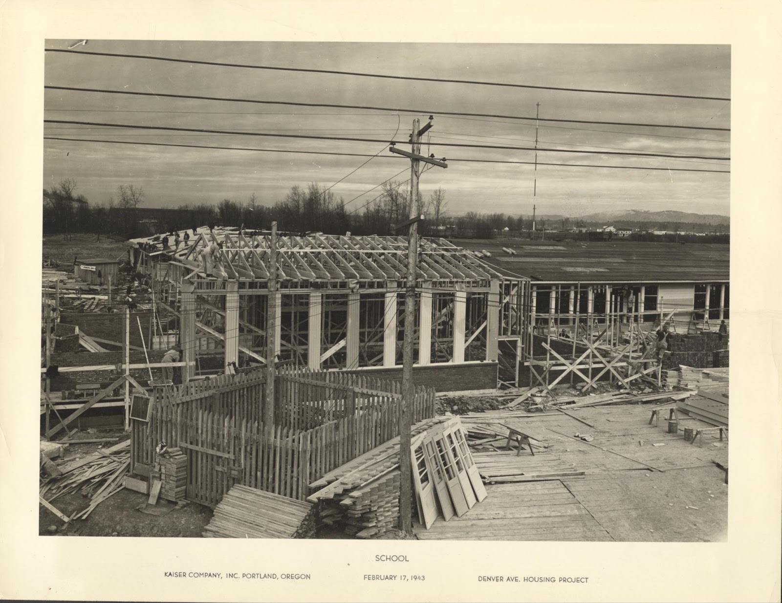 Sepia image depicting the construction site of a school building. Typed on the image is: School, Denver Ave. Housing Project, Feb. 17, 1943, Kaiser Company Inc. Portland, Ore.