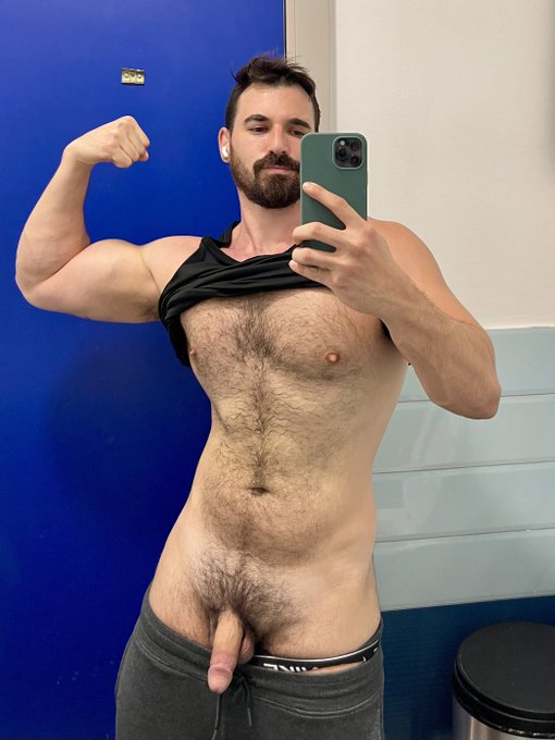 Thick Macho posing for an iphone mirrow selfie with his black tank top pulled up and his pants pulled down to reveal his flaccid cut penis