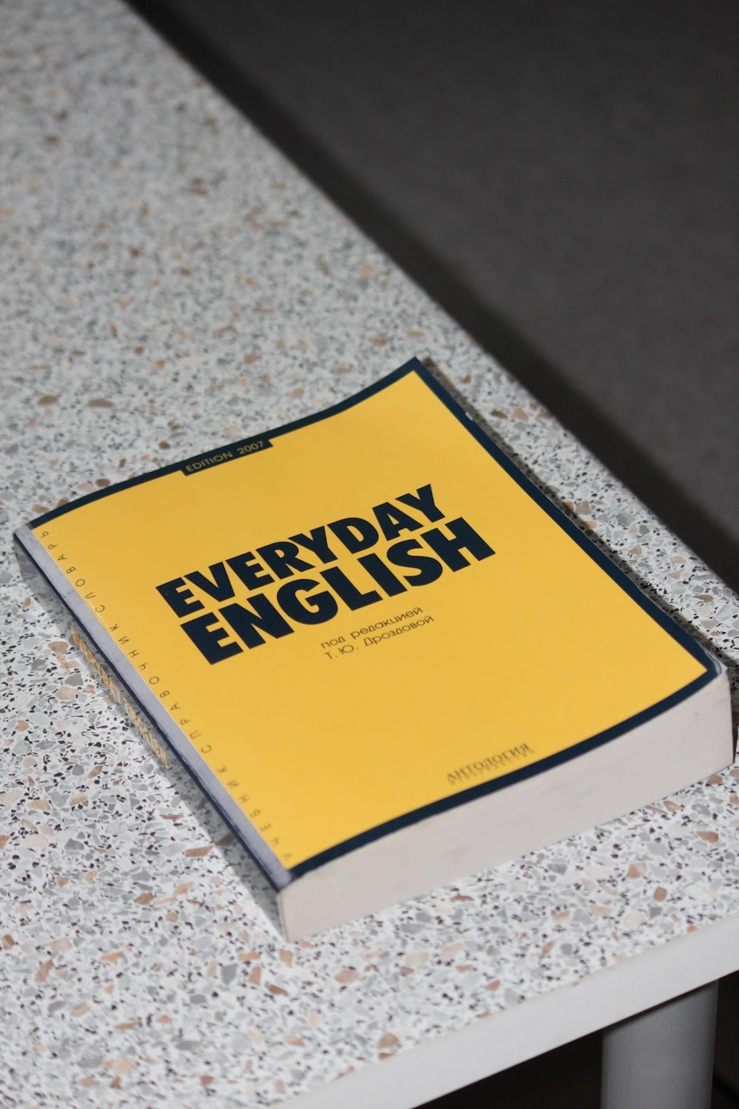 La imagen muestra a un libro amarillo en una mesa de mármol. El libro tiene el título “Everyday English”, que significa “Inglés cotidiano”.