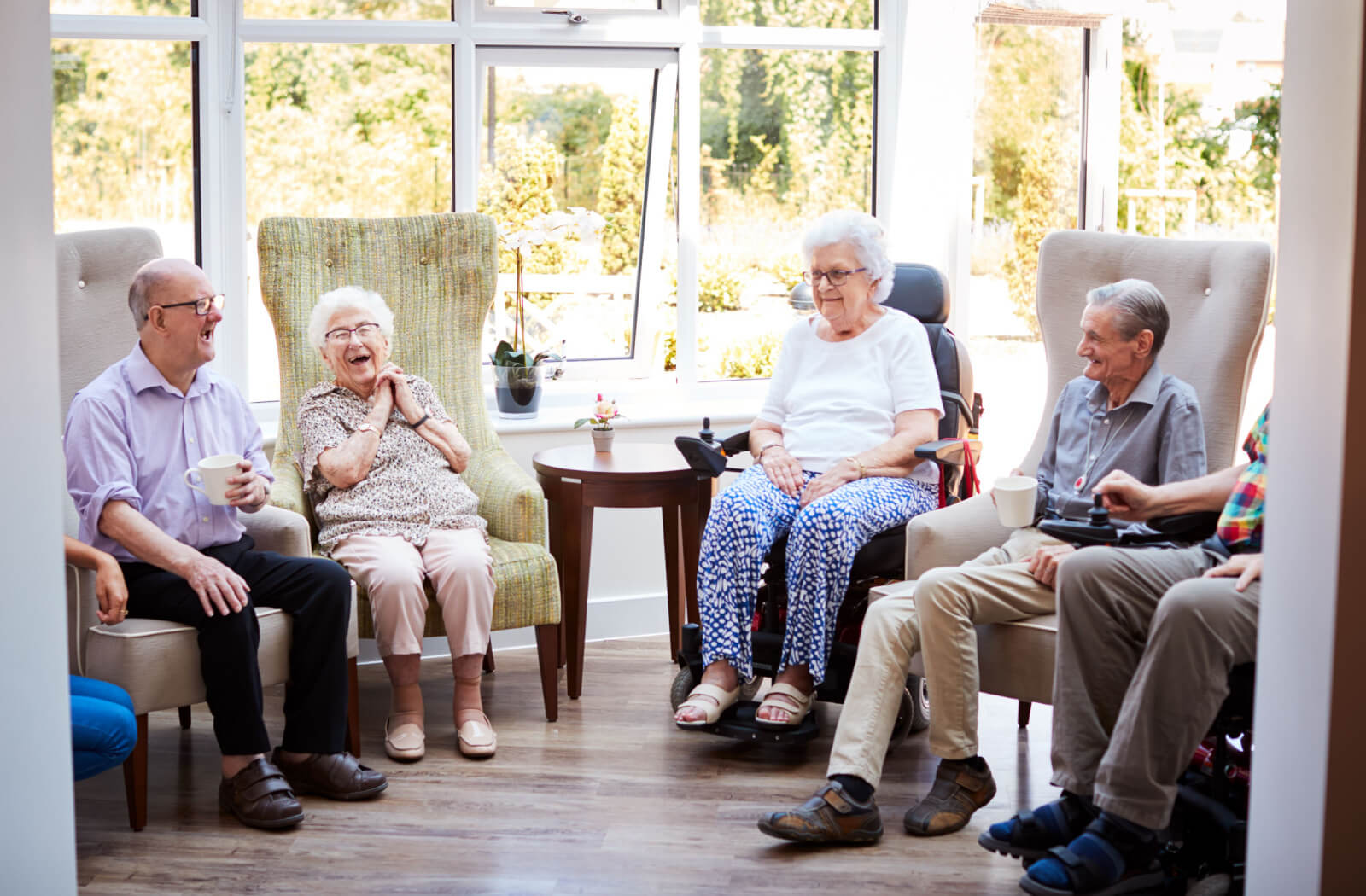 A group of seniors sitting talking to each other and having a cup of tea in a home care setting.