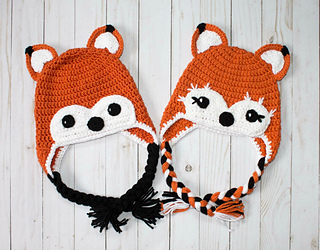 two crochet fox hats lying flat on white wooden background