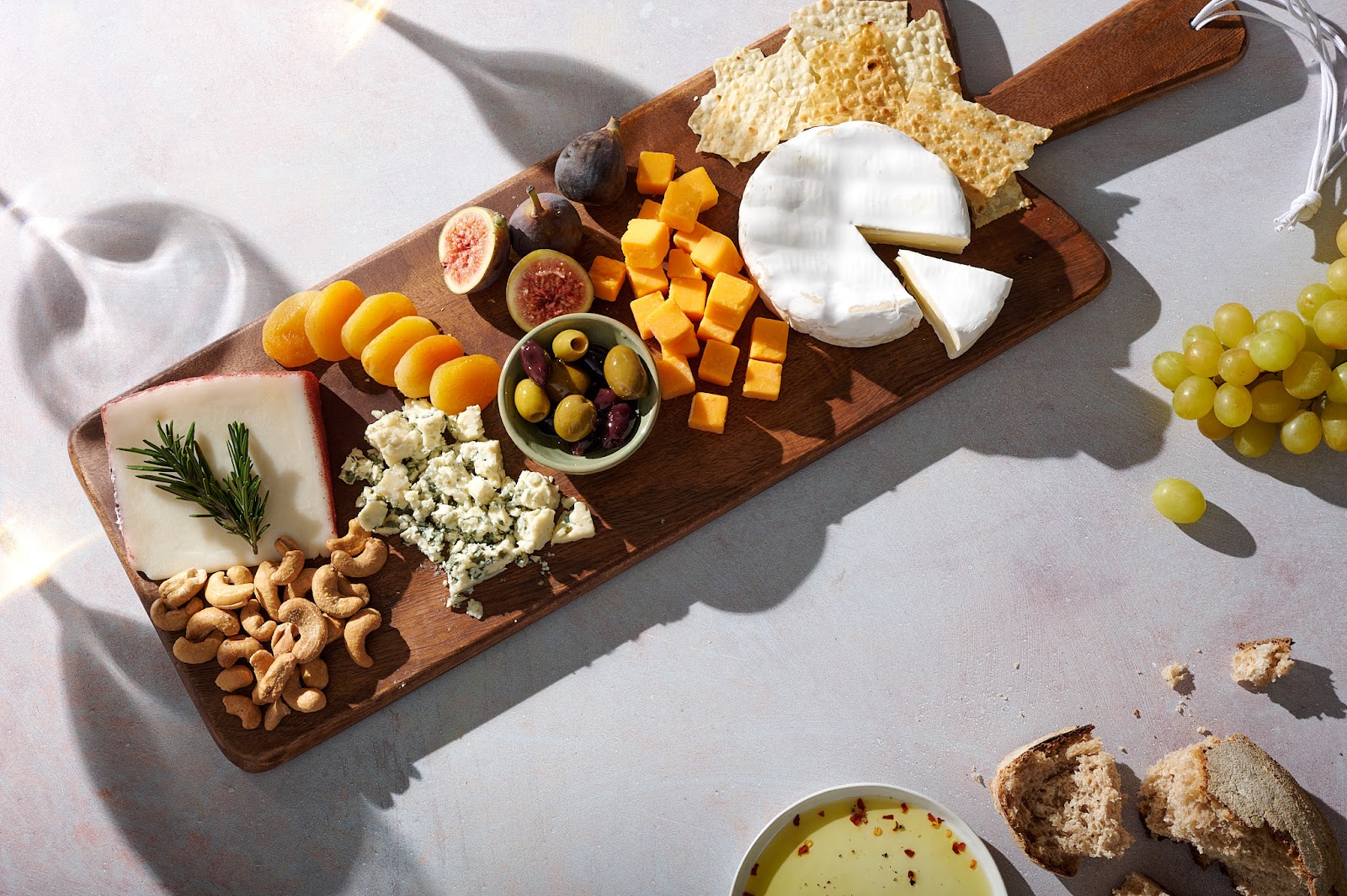 Cheeseboard setup on pink-hued table with wine glass shadows.