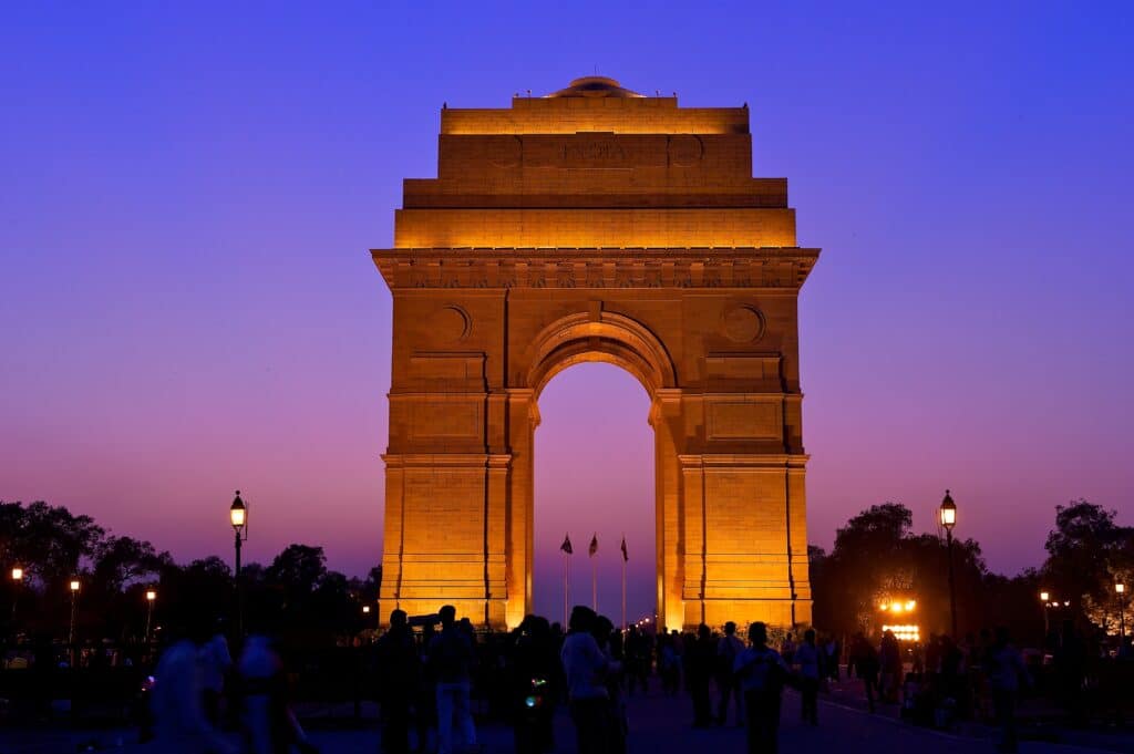 a large stone arch with lights at night with India Gate in the background