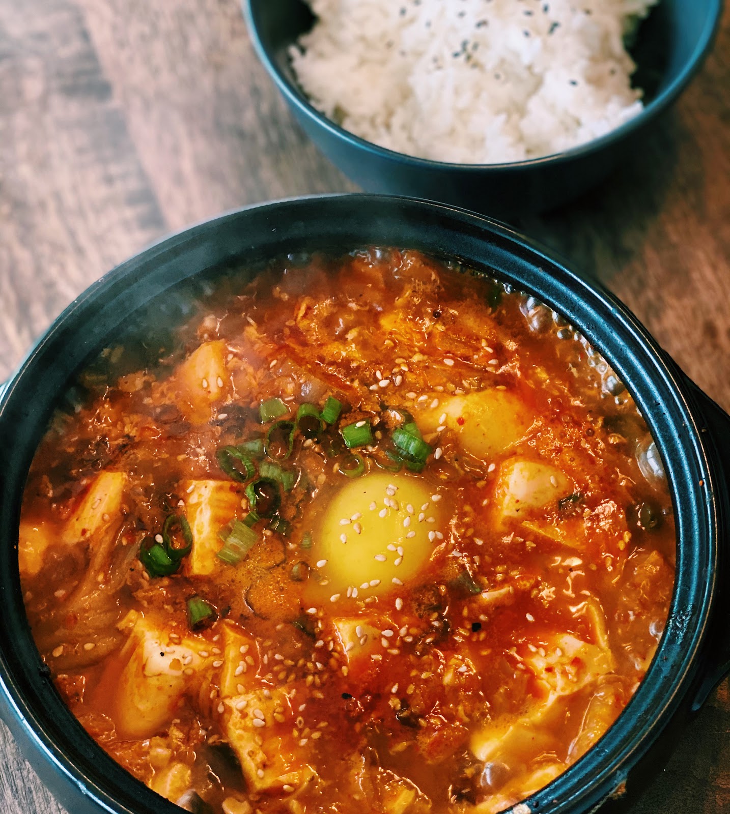 A bowl of hearty Kimchi Tofu Stew, rich in color with kimchi, tofu, and egg, garnished with green onions, ideal for a quick and healthy meal.