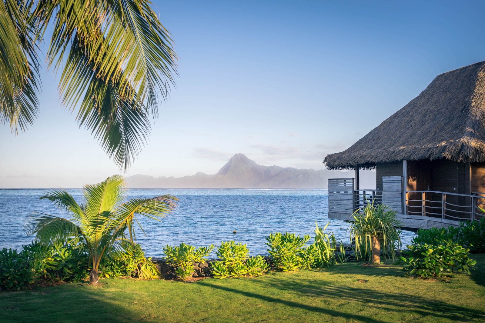 An overwater bungalow with turquoise waters below and mountains in the distance. 
