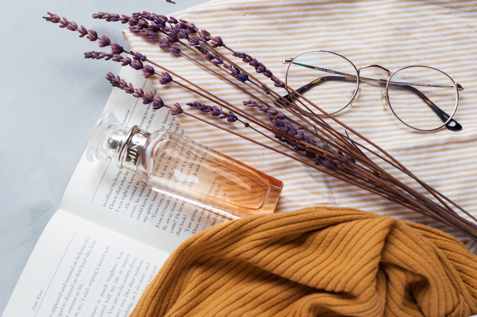 Una boccetta di profumo appoggiata sul libro con alcune decorazioni come occhiali e sciarpa