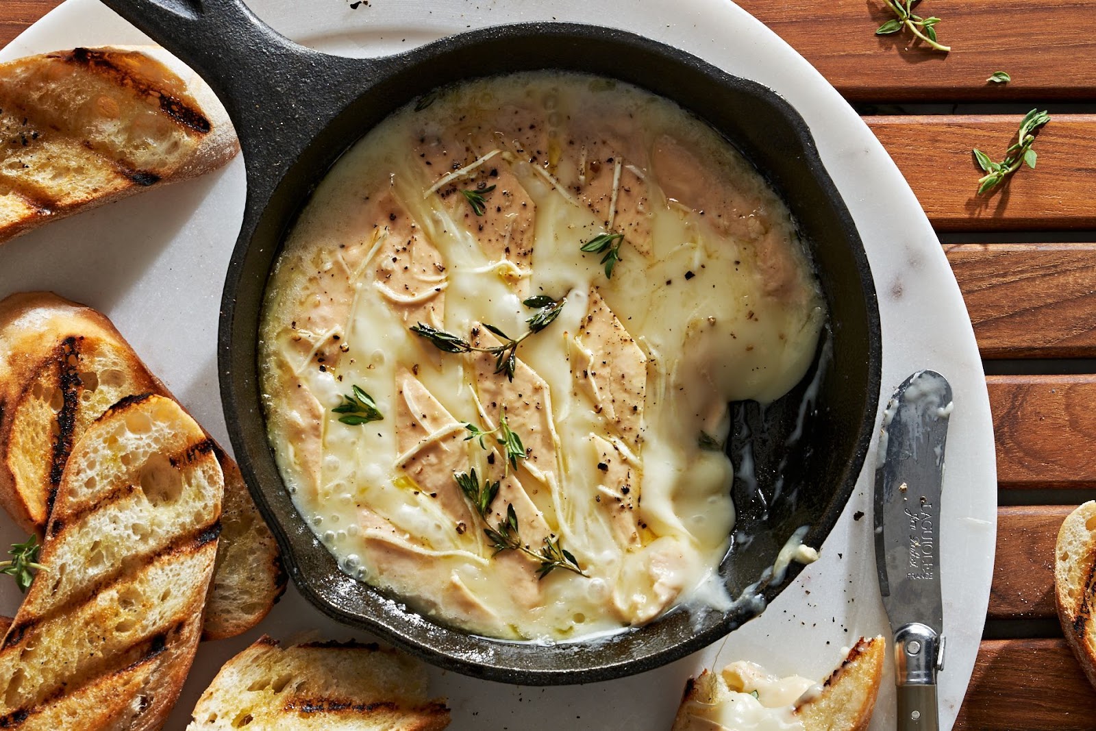 Grilled brie in a cast iron frying pan with toasted bread served on a plate.