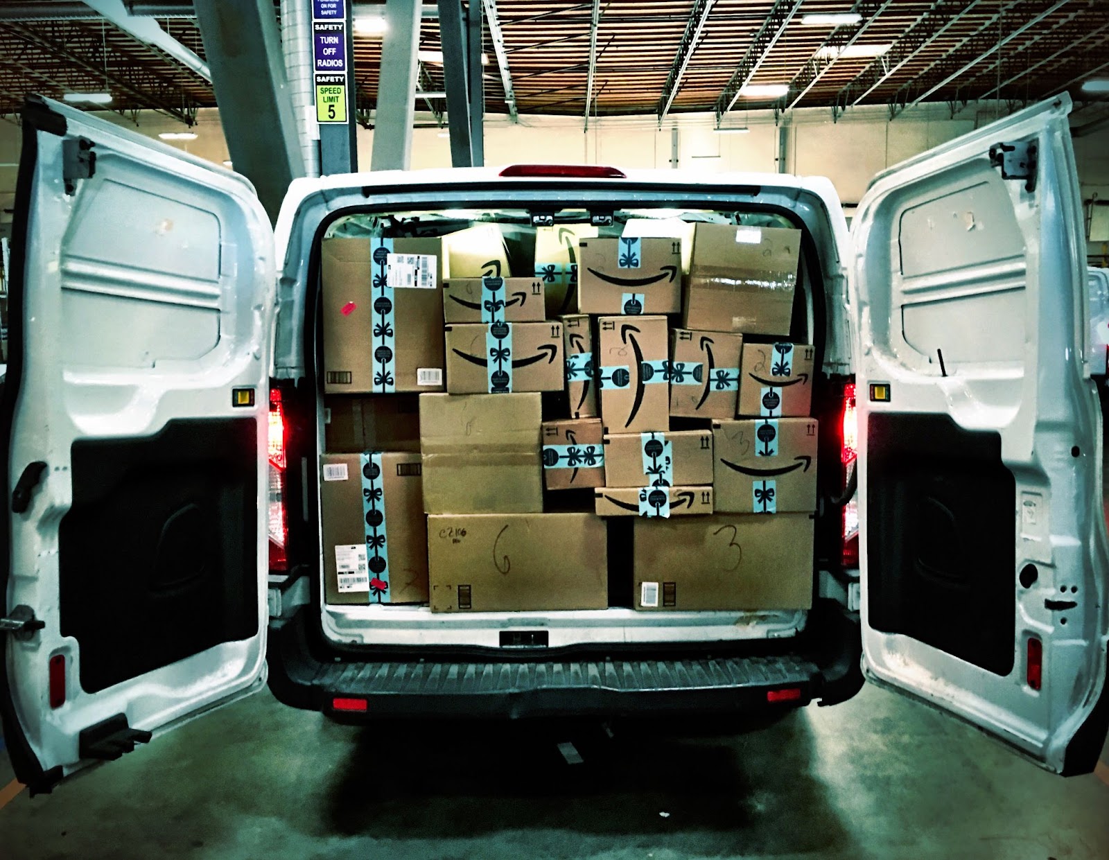 An delivery vans back doors open showing it filled with Amazon boxes