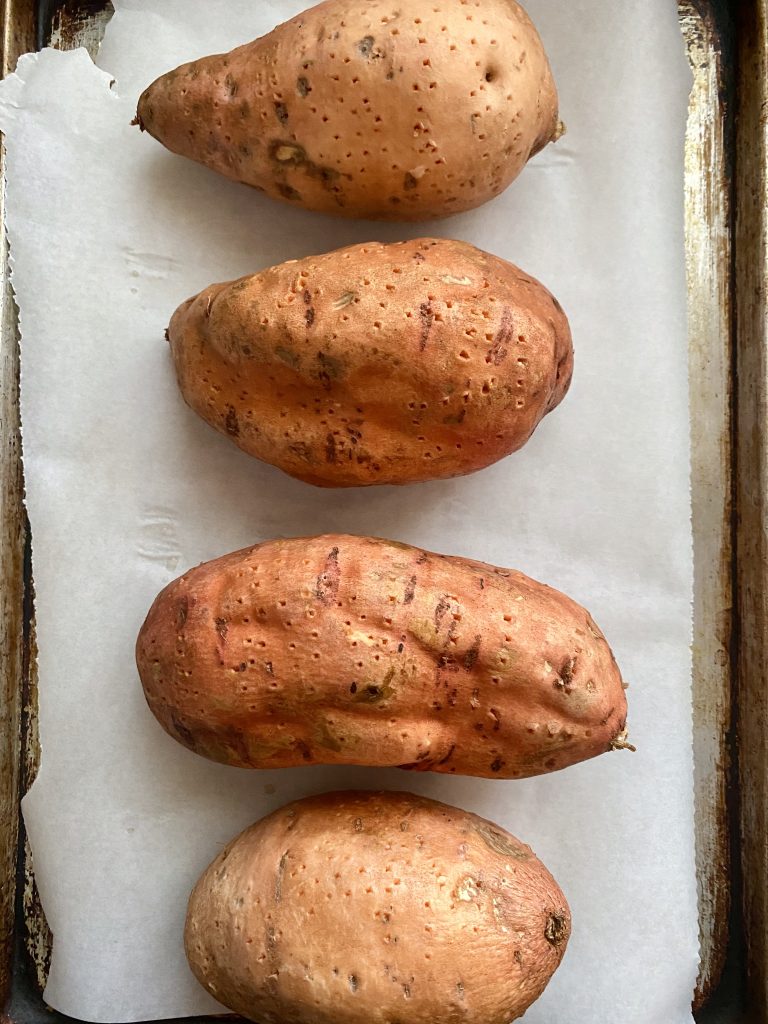 Raw whole sweet potatoes pierced with a fork on a cooking tray