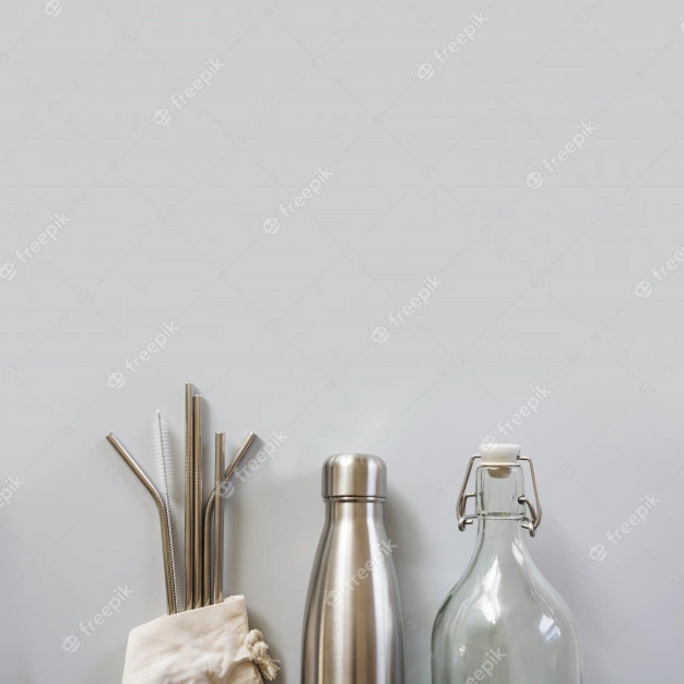 #DescriçãoDaImagem: foto com fundo neutro e no canto inferior aparece uma parte de canudos reutilizáveis, garrafa de alumínio e garrafa de vidro. Foto: Freepik