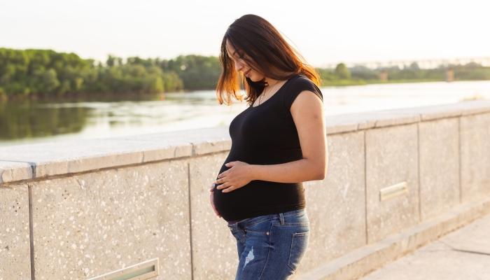 Portrait of hispanic pregnant woman walking in a curb at sunset.