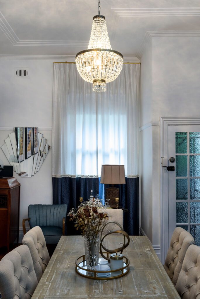 Cozy dining area with a rustic wooden table, decorated with a centerpiece of dried flowers. The room features elegant tufted chairs, a sparkling chandelier, and a mix of modern and vintage decor.