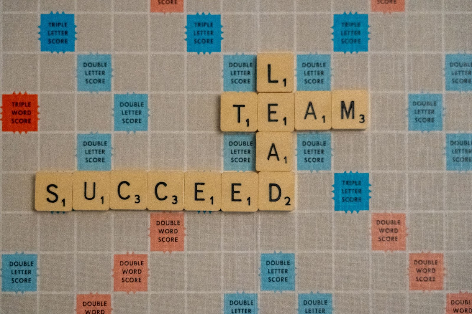 A scrabble board with the words: succeed, lead, and team