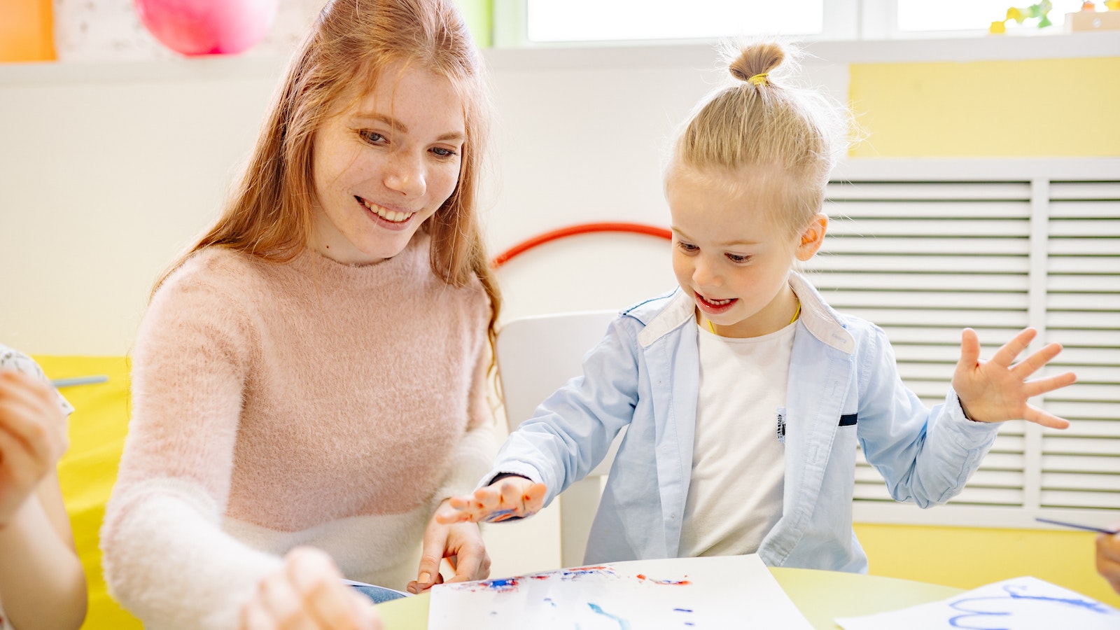 Girl learning to paint with a childcare worker