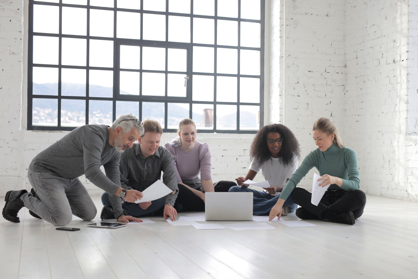 Bunch of people sitting on a white wooden floor, possibly discussing a project
