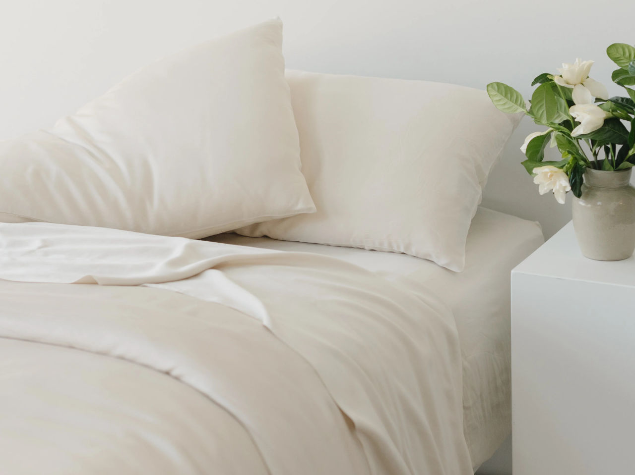 Bed with off-white sheets next to plant