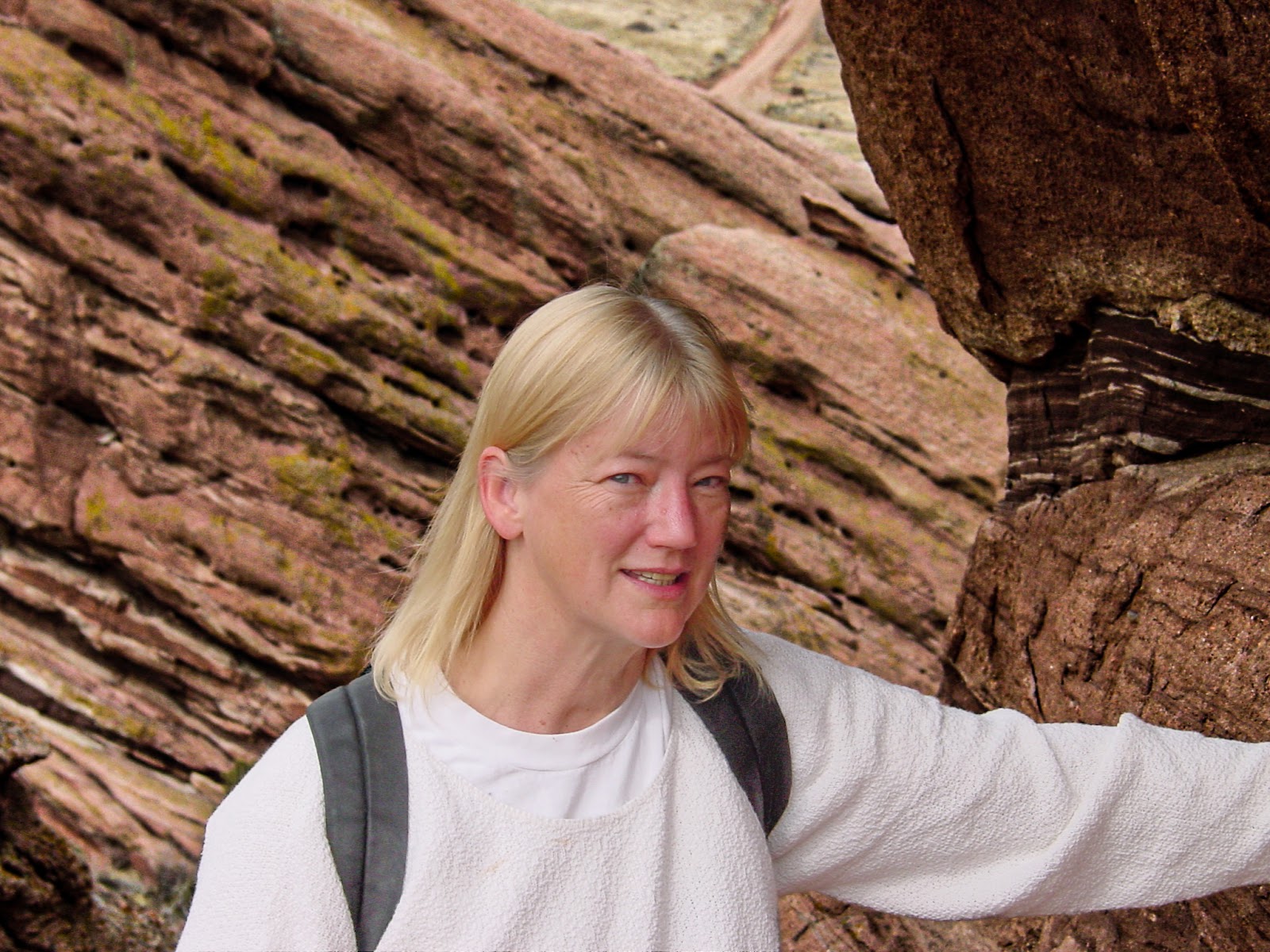 Woman leans on huge red rock with rocky landscape behind.