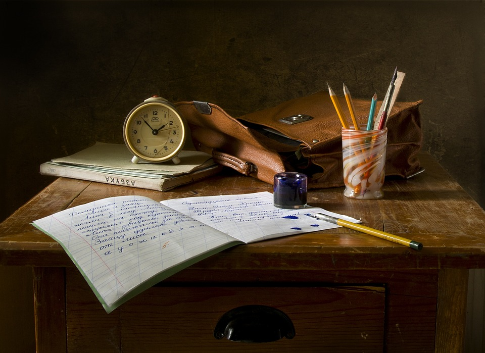 Study book open on a table with pen, books and a clock