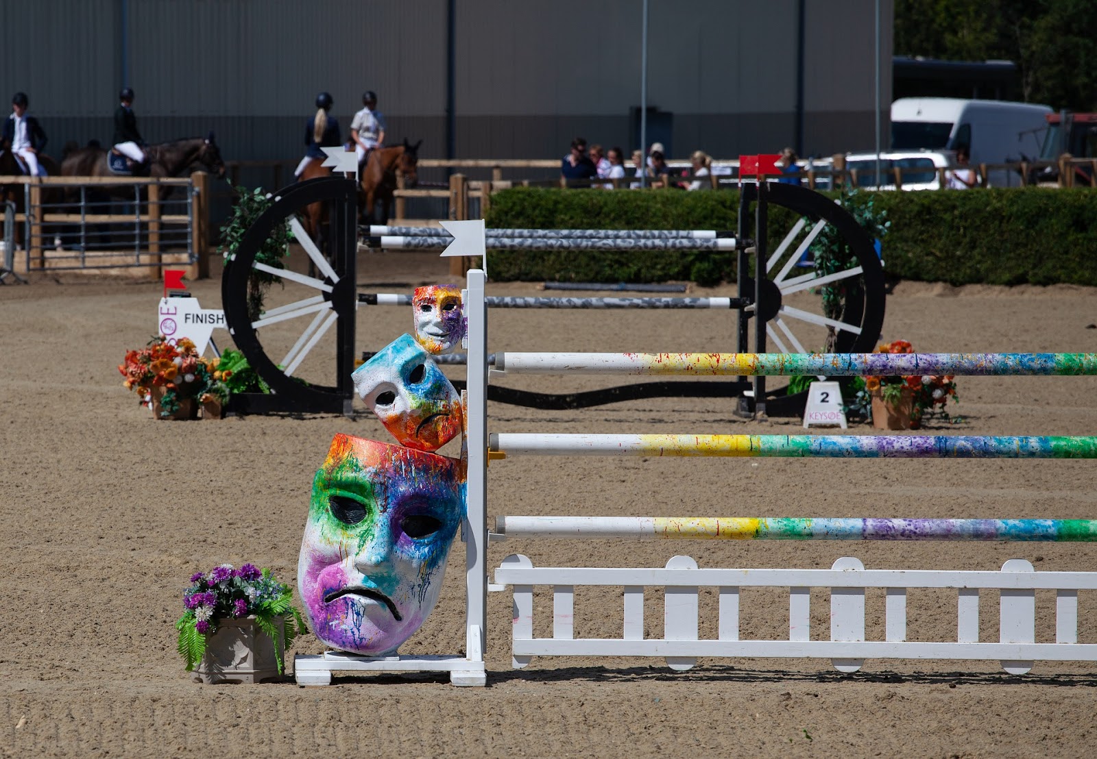 A bright vertical and dark oxer jump combination in a sand riding ring. 