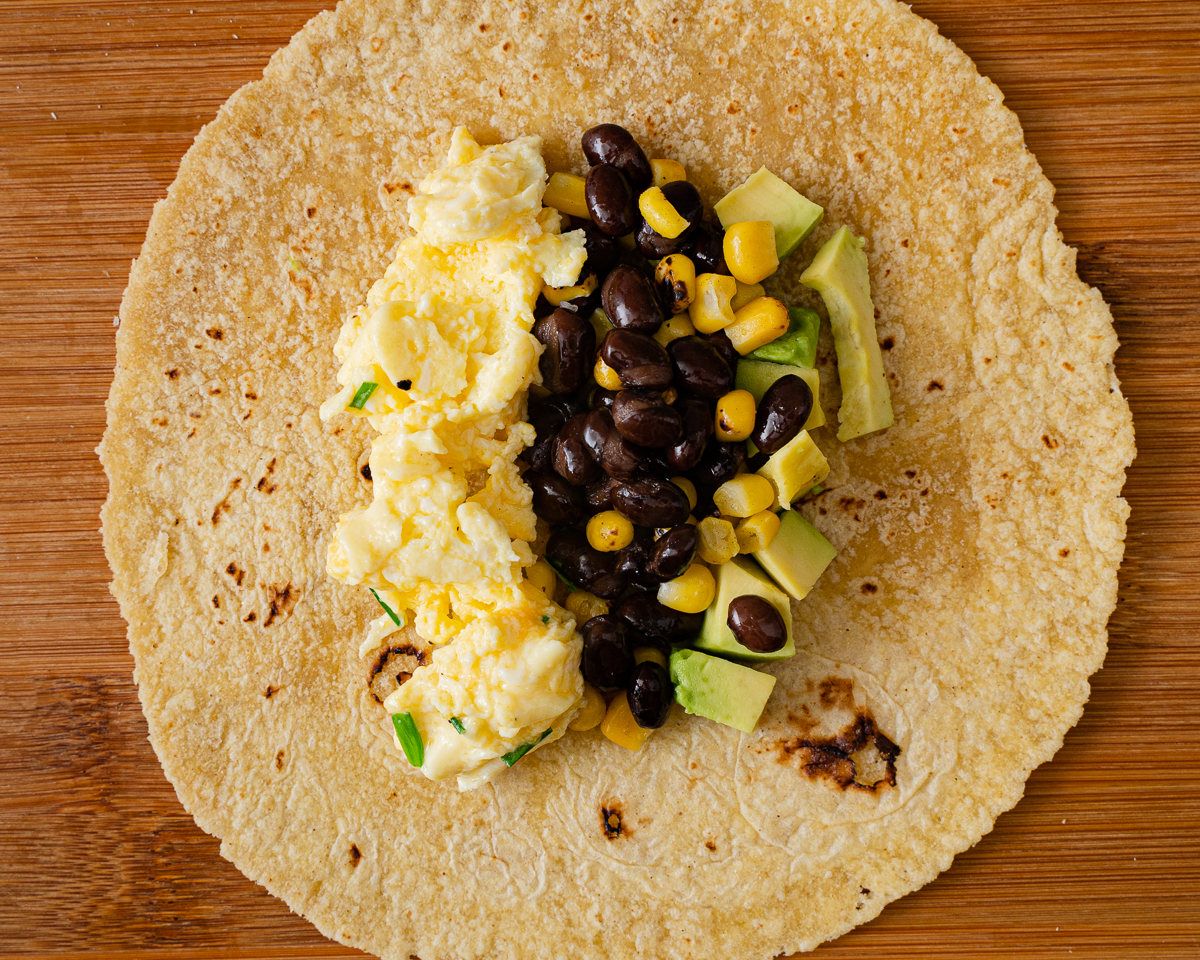 avocado, beans, corn, scrambled egg lay on a tortilla