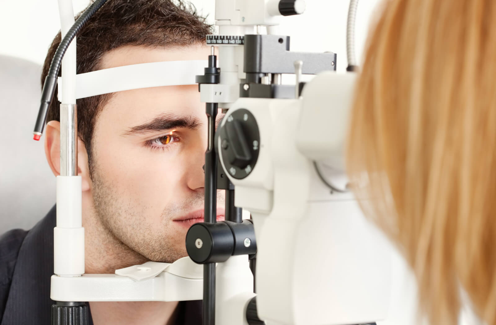 Close-up of a  young man sitting in an optometrist office looking into a machine that tests his vision.