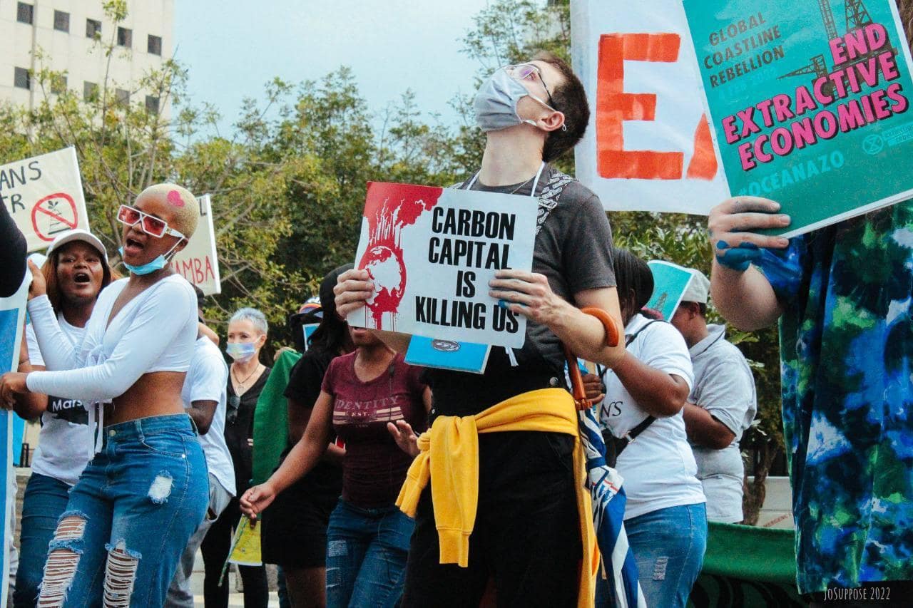 Young people march and chant along a Johannesburg street holding banners. One says 'Carbon Capital Is Killing Us'. Another 'End Extractive Economies'