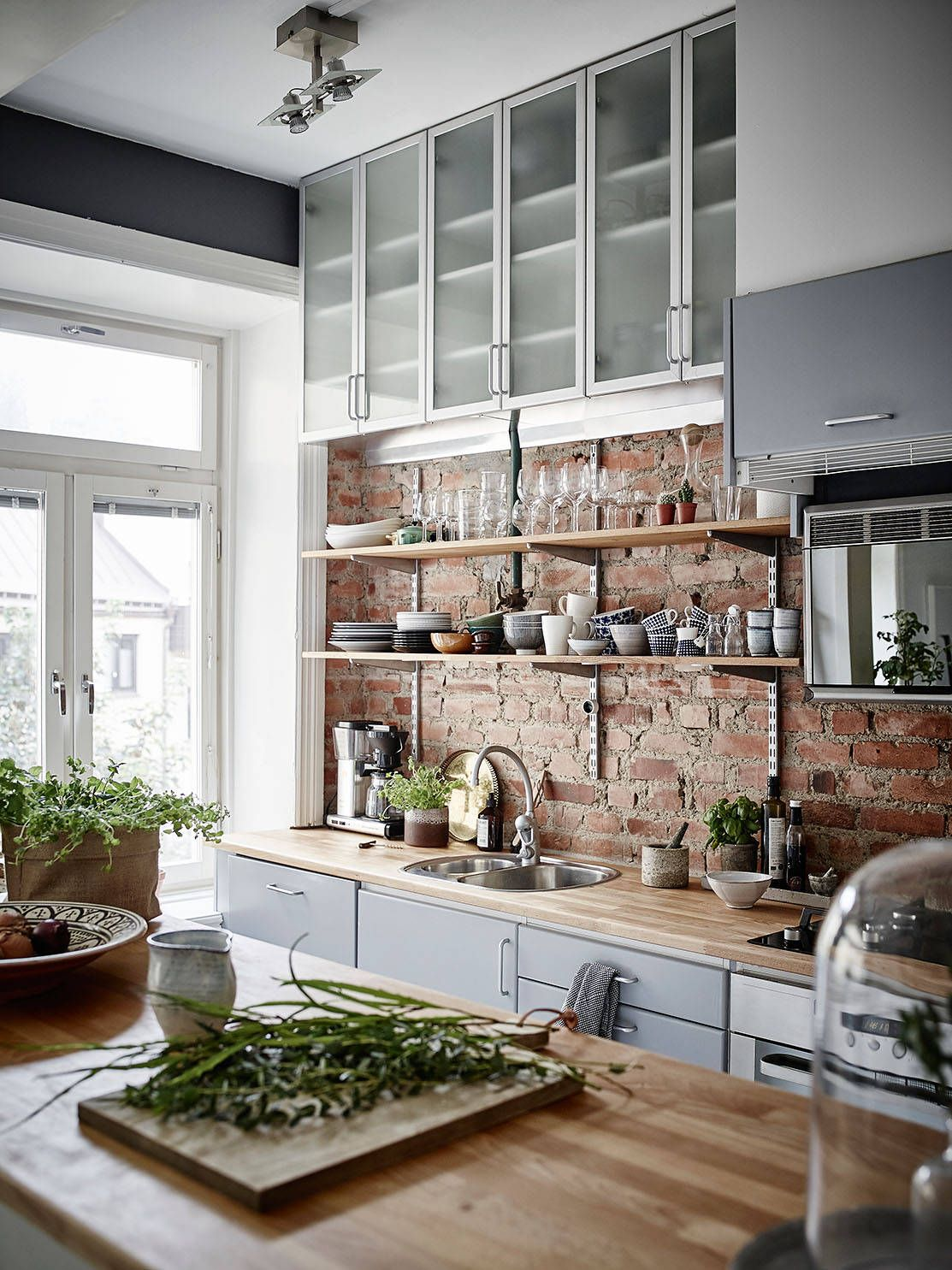 scandinavian kitchen with original brick backsplash, butcher block countertops, a center island for food prep and glass front kitchen cabinets