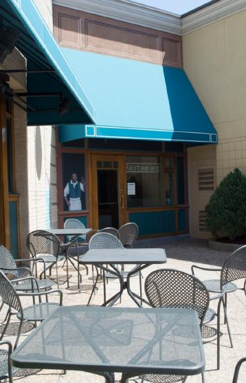 Exterior of a building with blue awnings and black metal chairs and tables