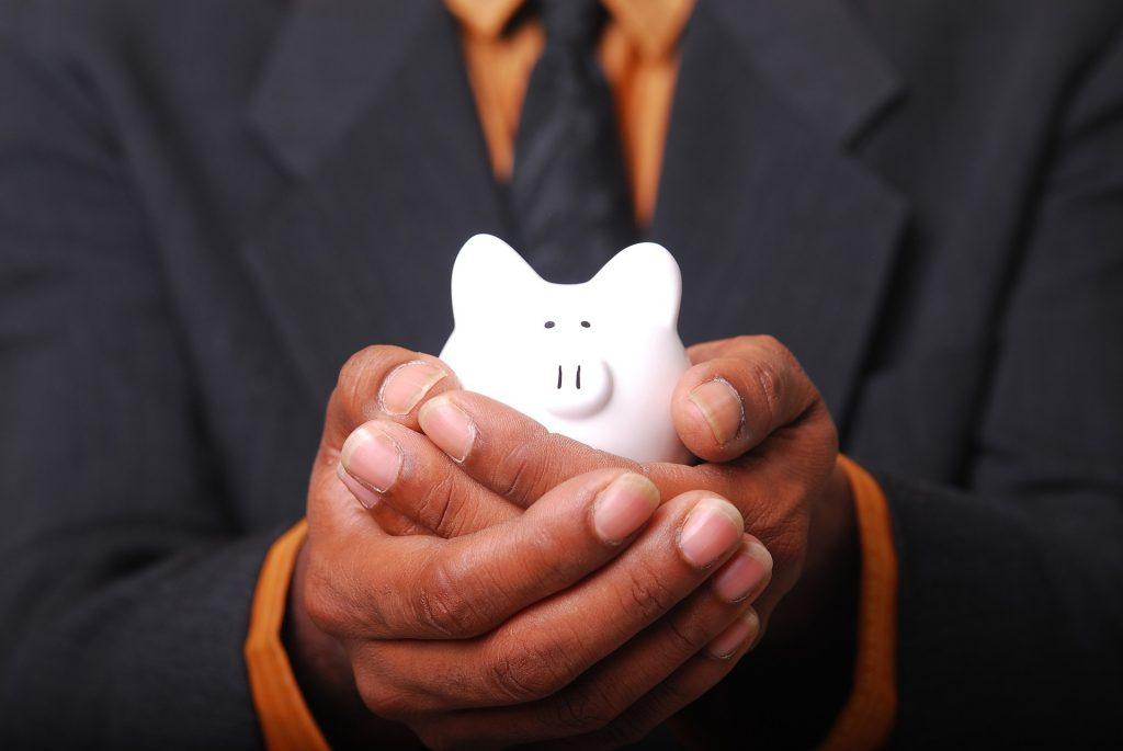 A man in a black suit jacket and orange shirt holding a white piggybank.