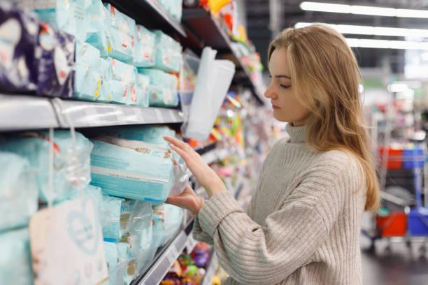 Young woman mother chooses diapers at supermarket in shop mall. Hygiene products for children Young woman mother chooses diapers at supermarket in shop mall. Hygiene products for children women diapers stock pictures, royalty-free photos & images