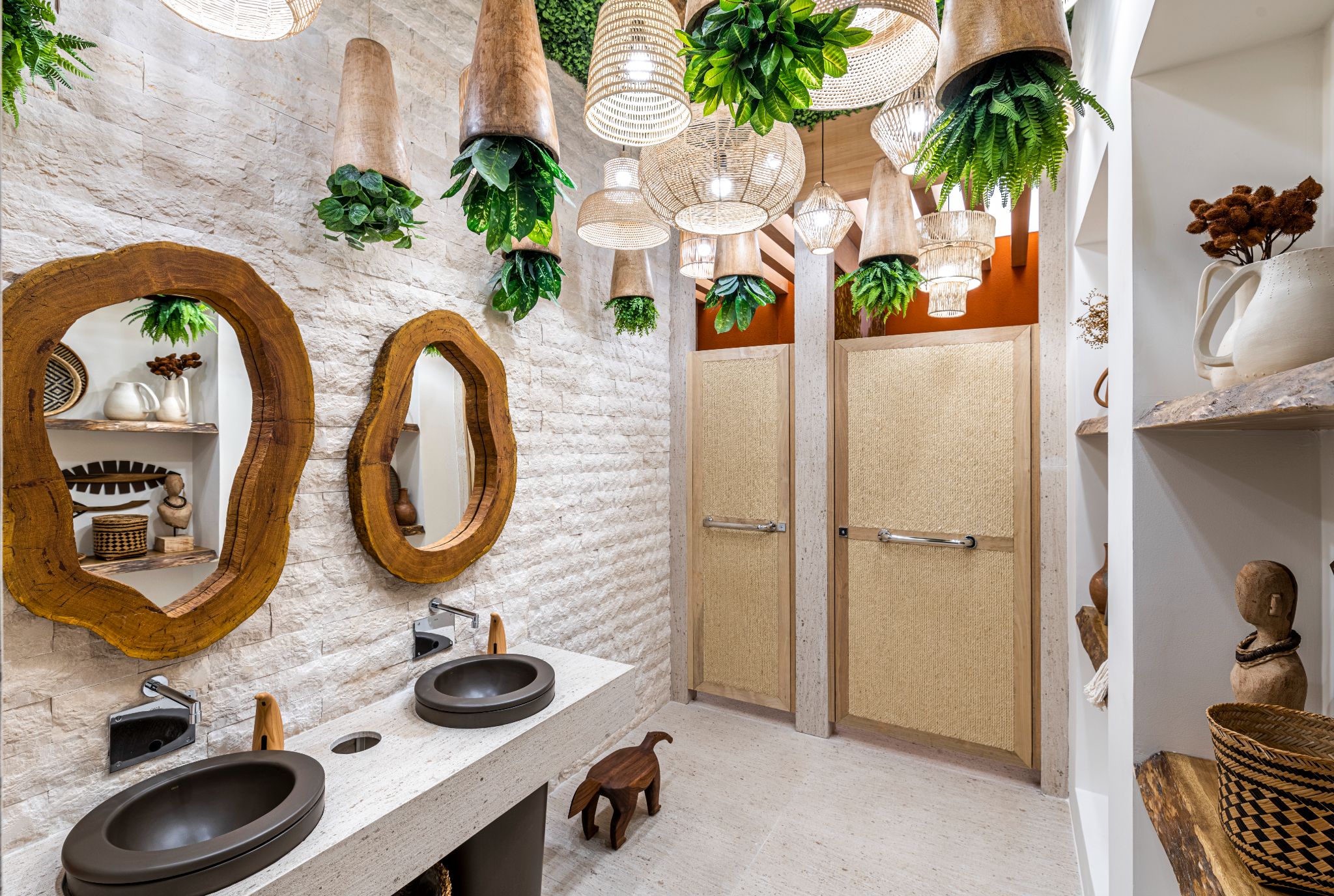 Banheiro com parede de pedras egípcias irregulares, as luminárias de fibras naturais e as plantas pendentes em cúpulas de madeira.
