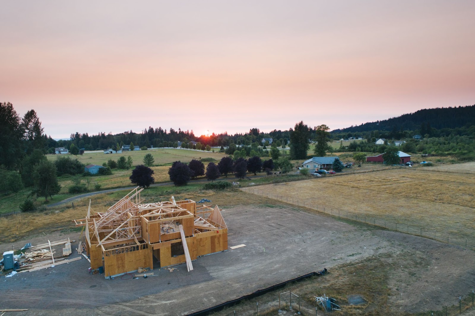 frame of new home being built with sunset behind trees in the background