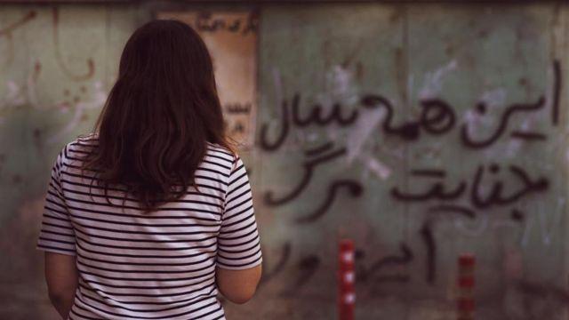 زنی بدون حجاب مقابل دیواری که رویش شعار نوشته شده است