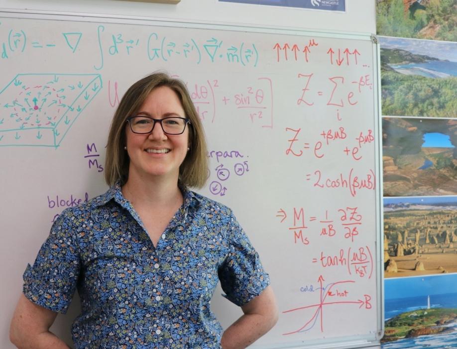 Dr Karen Livesey stands in front of a whiteboard, which is covered in physics equations
