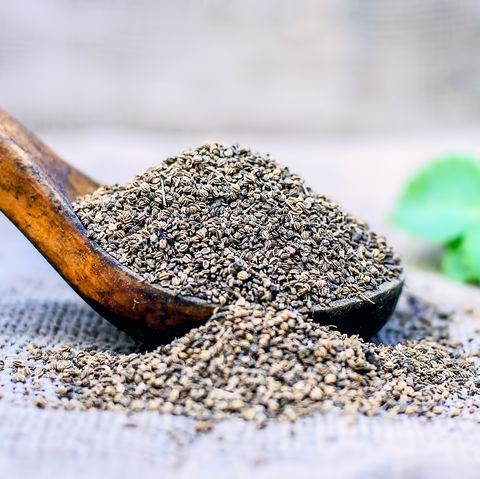 Trachyspermum ammi, Ajwain hạt trong một muỗng gỗ với một số lá trên nền màu xanh lá cây.