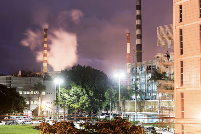 A imagem parte da prefeitura municipal da cidade de Ipatinga, assim como o pátio e outros prédios. Ao fundo, é possível ver grandes chaminés da Usiminas.