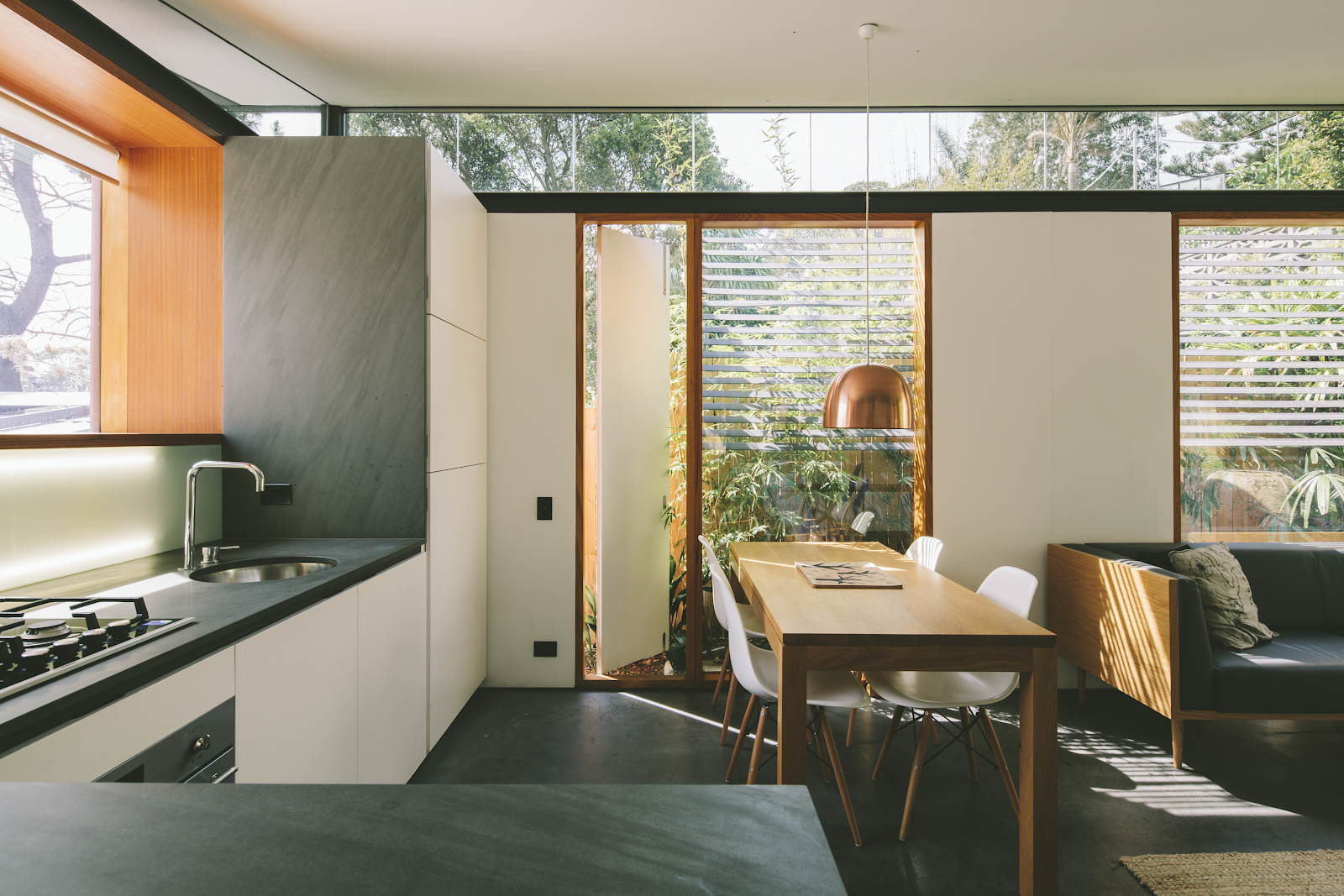 modern australian home with adjoining kitchen and living room. white flat panel cabinets are simple yet elegant. grey countertops and large windows surround them