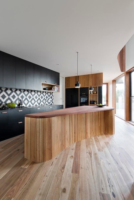 modern kitchen with rounded island, black cabinets, geometric backsplash and wood floor