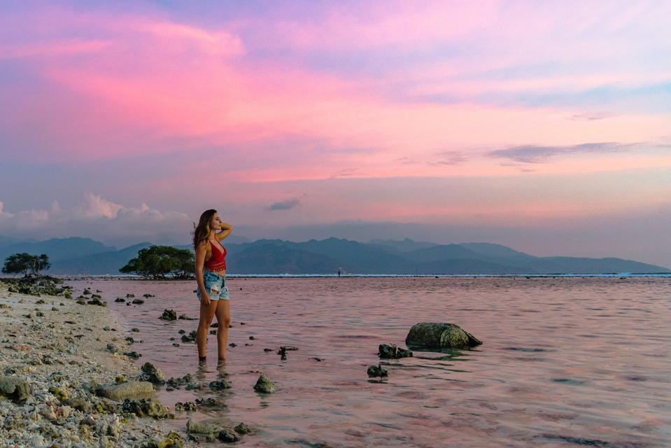 attractive woman looking out into pink sunset by the beach in indonesia