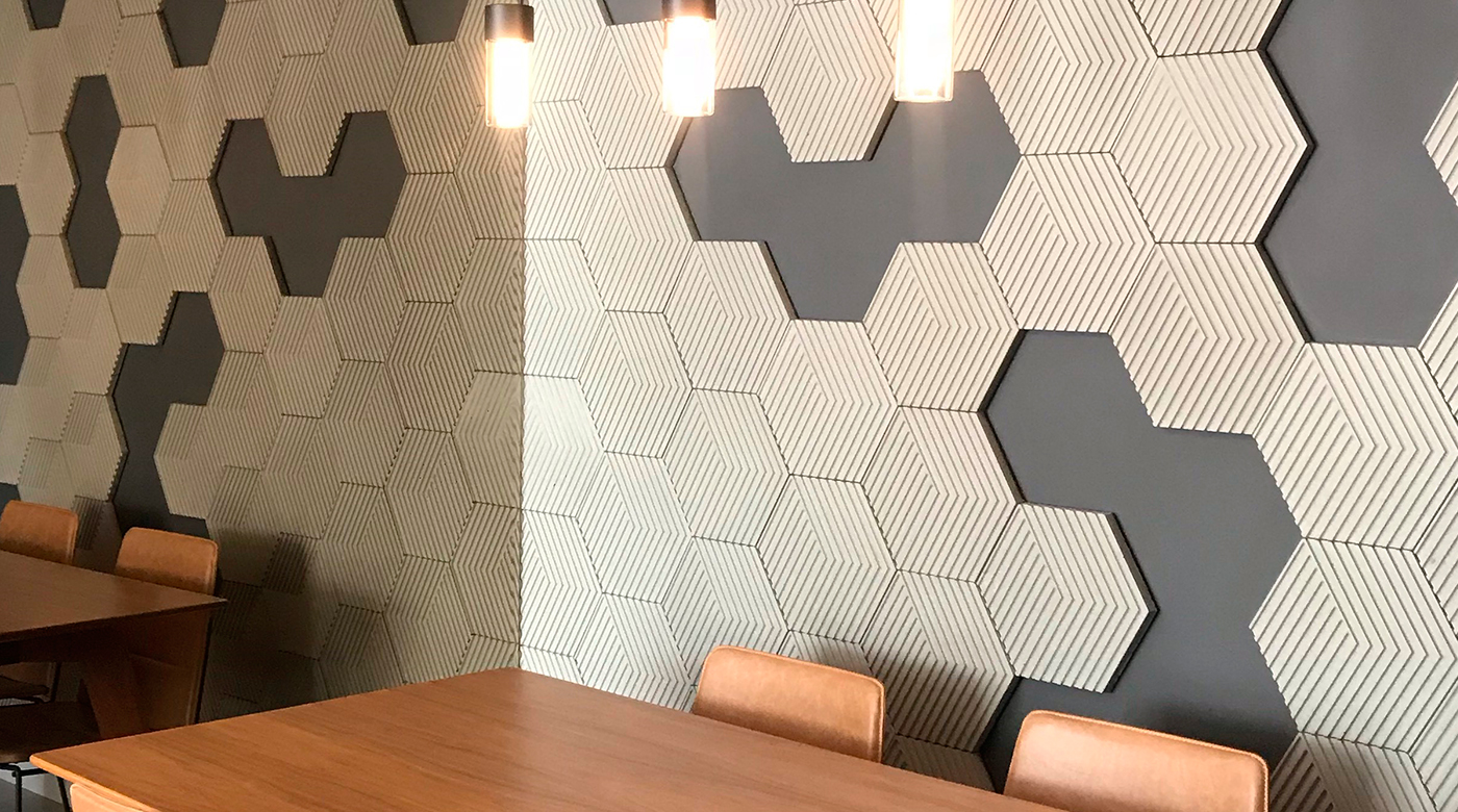 Ambiente com mesa de madeira, luminária pendente e parede com revestimento hexagonal em 3D.