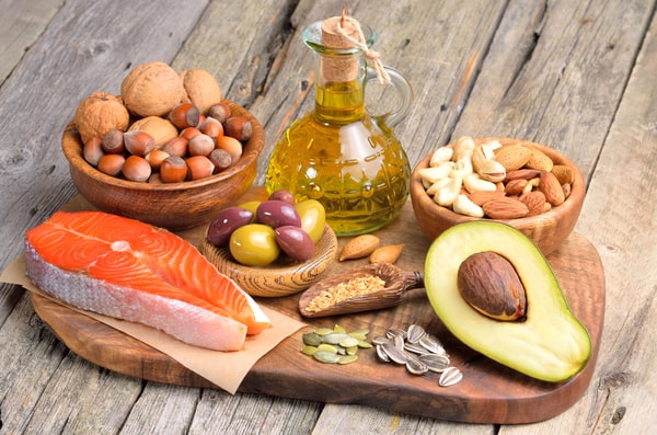 Nuts in wooden bowls, healthy oil in a bottle, half avocado, fatty fish, and healthy seeds on a wooden board