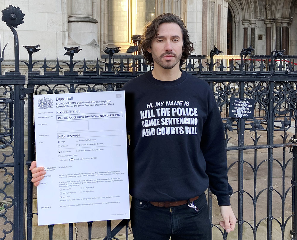 A young man stands outside the courts of justice in London. He holds up a deed poll that shows he is now legally named Kill The Police Crime Sentencing and Courts Bill.