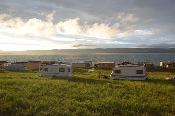 Beautiful picture with RVs and small houses on grass with sea and mountain on sight