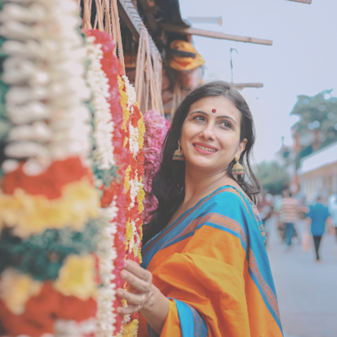 Woman in a saree posing against garlands of flowers
