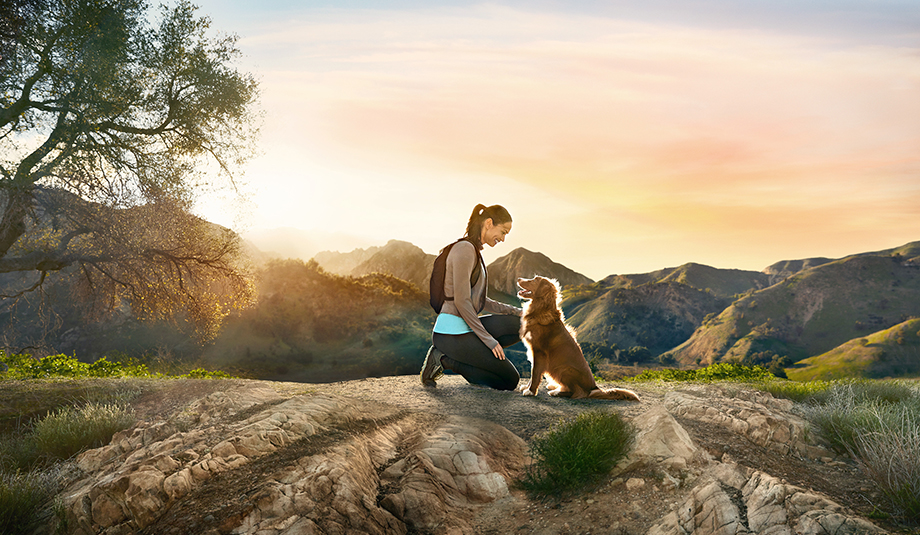 Hero image of woman and dog looking at each other silhouetted by a pink and orange sunset. Shot by Lou Bopp in the Santa Monica Mountains for Purina Pro Plan's recent campaign. 