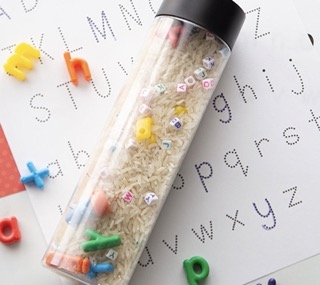 A rice sensory bottle with a black lid placed on a white paper with letters of the alphabet. 