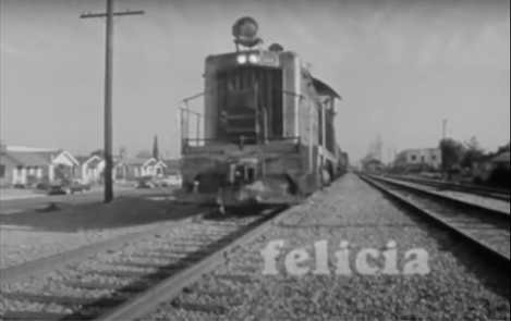 Title card, Felicia (1965). A black-and-white wide shot of an old-fashioned train moving down a track through the LA neighbourhood. In the bottom left of the frame, the title "Felicia" in bold lower-case letters.
