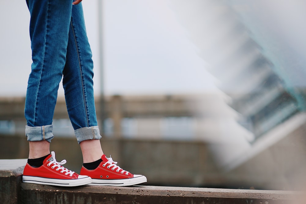 person in red Converse All-Star low-top sneakers standing on fence