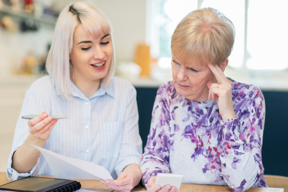 Young woman helping confused senior woman with financial paperwork.